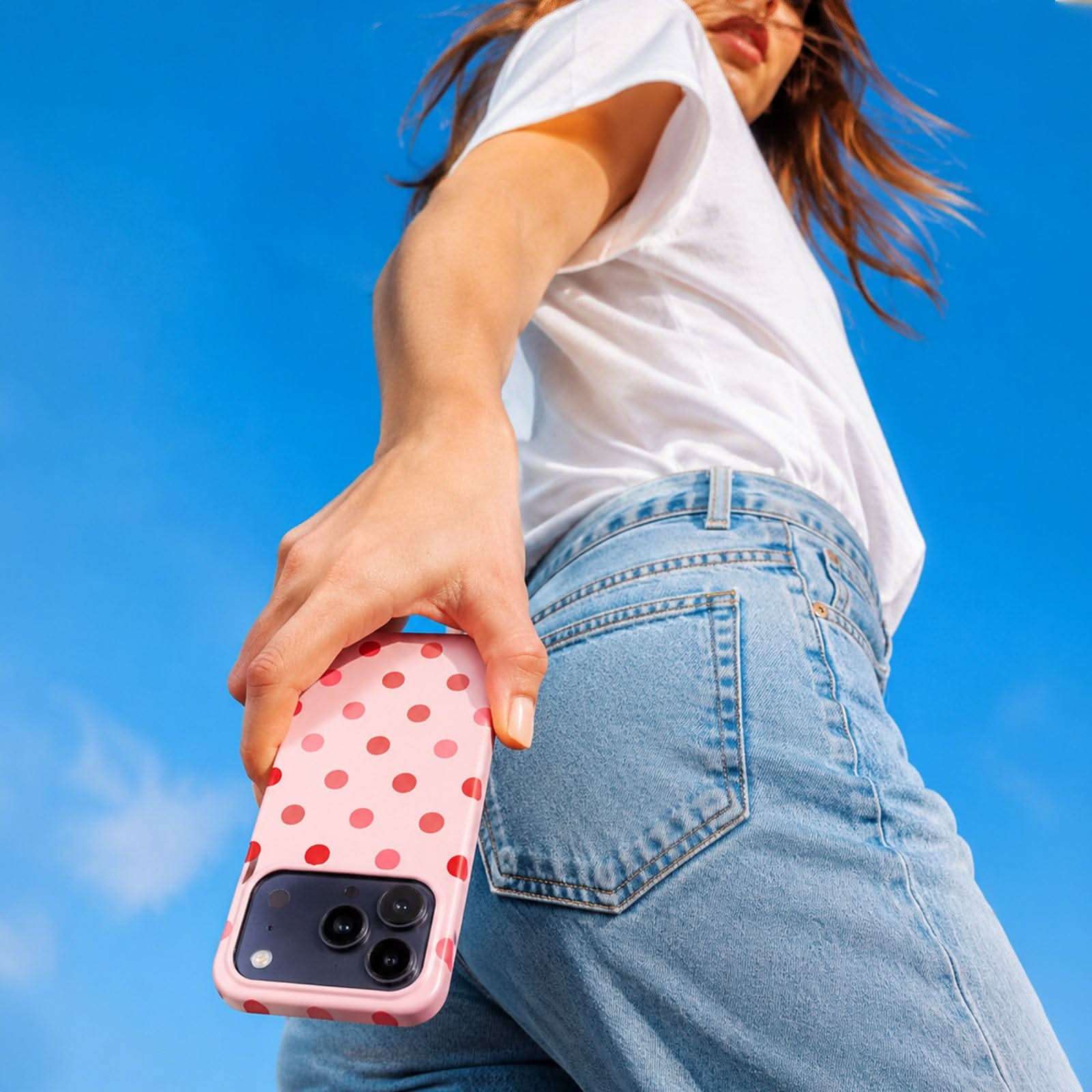 Cherry Blush MagSafe Tough Phone Case with red polka dots on pink, shown on iPhone against blue sky
