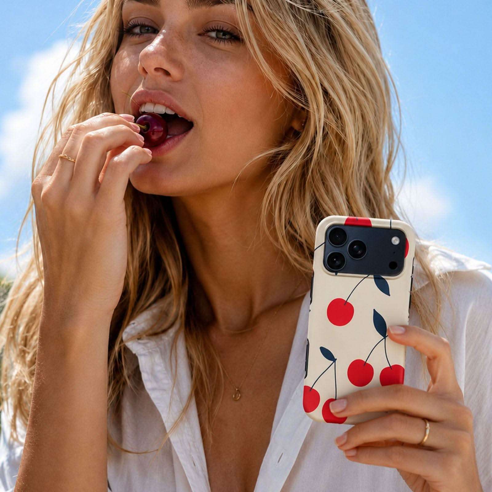 Cream Cherry MagSafe Tough Phone Case with red cherry pattern, shown on iPhone held by woman eating cherry outdoors.