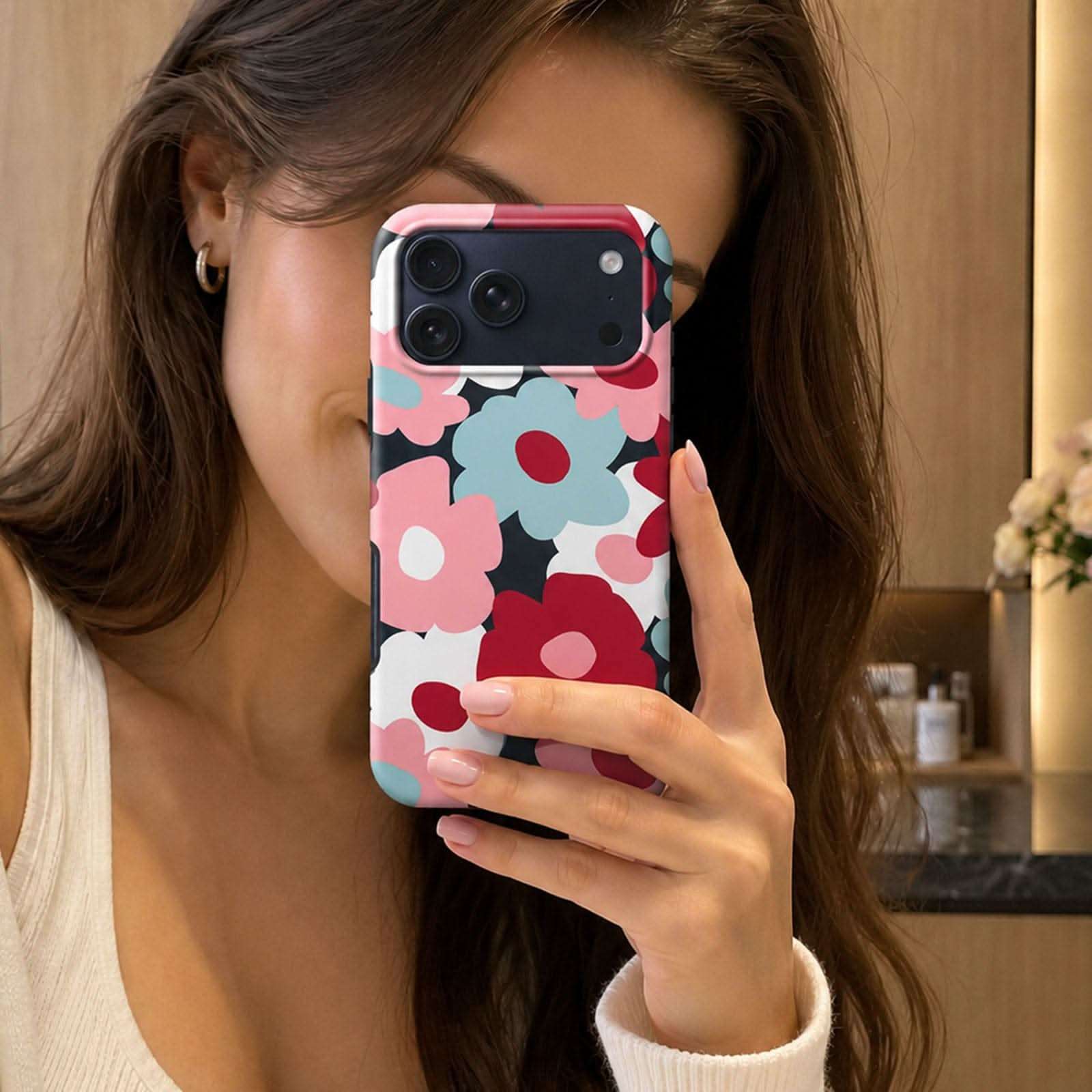 Colorful floral phone case with pink, blue, and burgundy flowers on dark background, held up in mirror selfie.