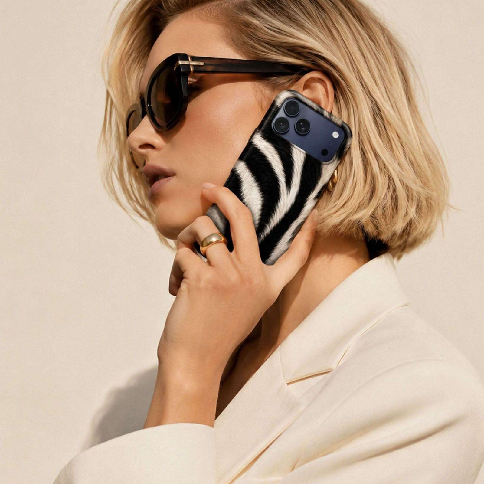 Zebra print phone case in black and white on blue iPhone, displayed on person wearing cream blazer and black sunglasses.