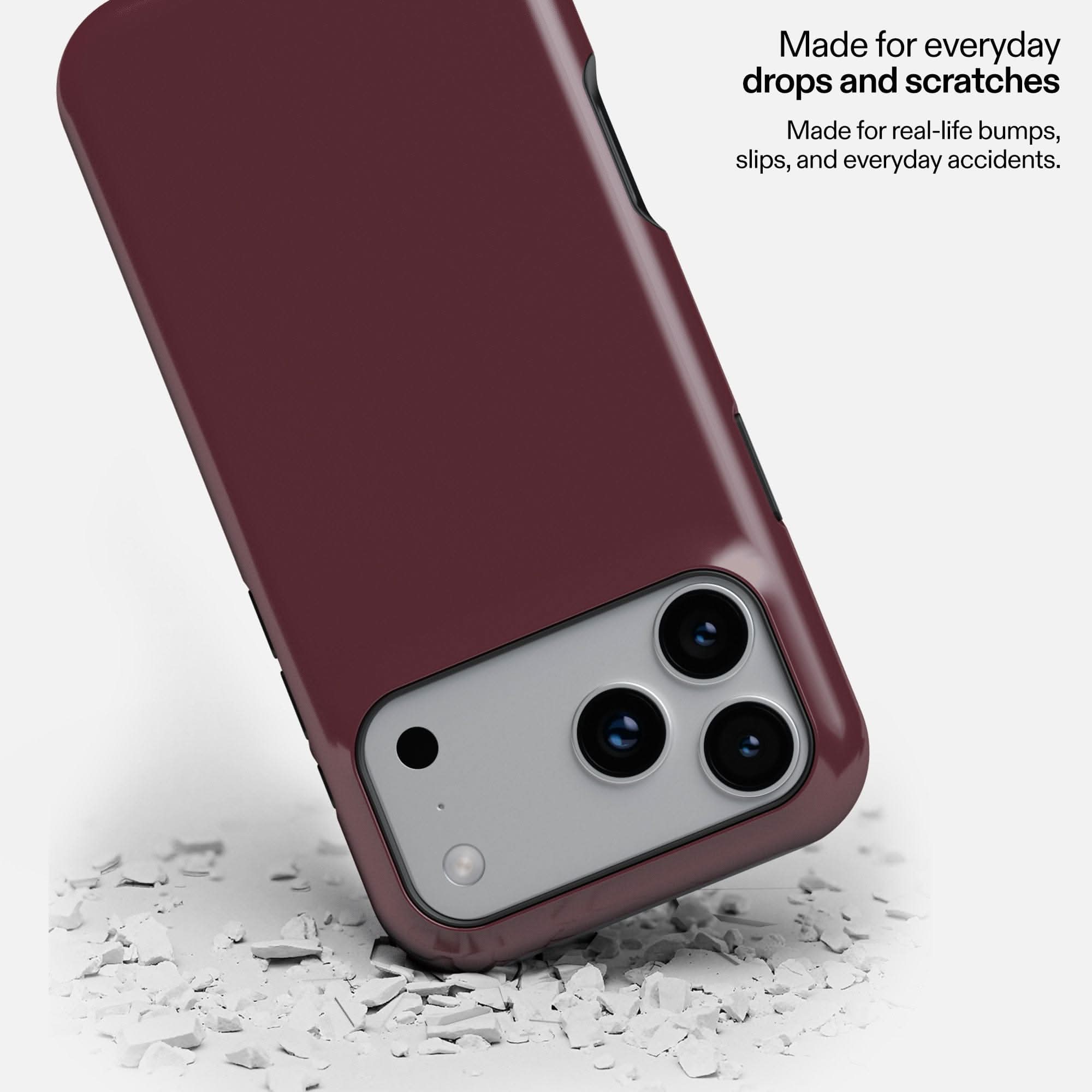 Deep burgundy MagSafe tough phone case with triple camera cutout, displayed on white debris surface.