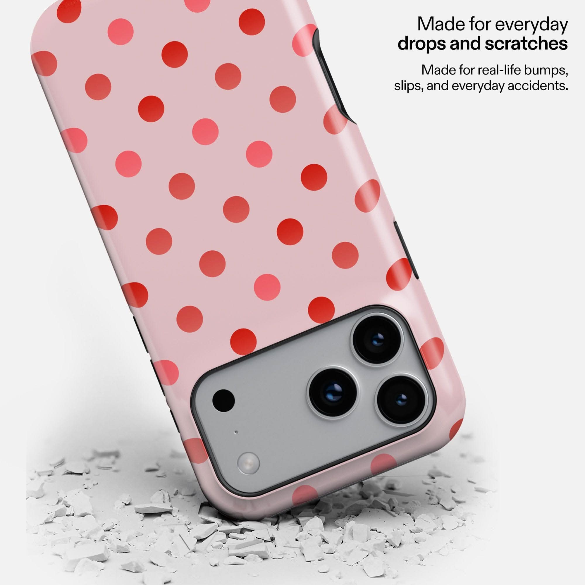 Pink phone case with red polka dots, dropped on white debris, showing triple camera setup.