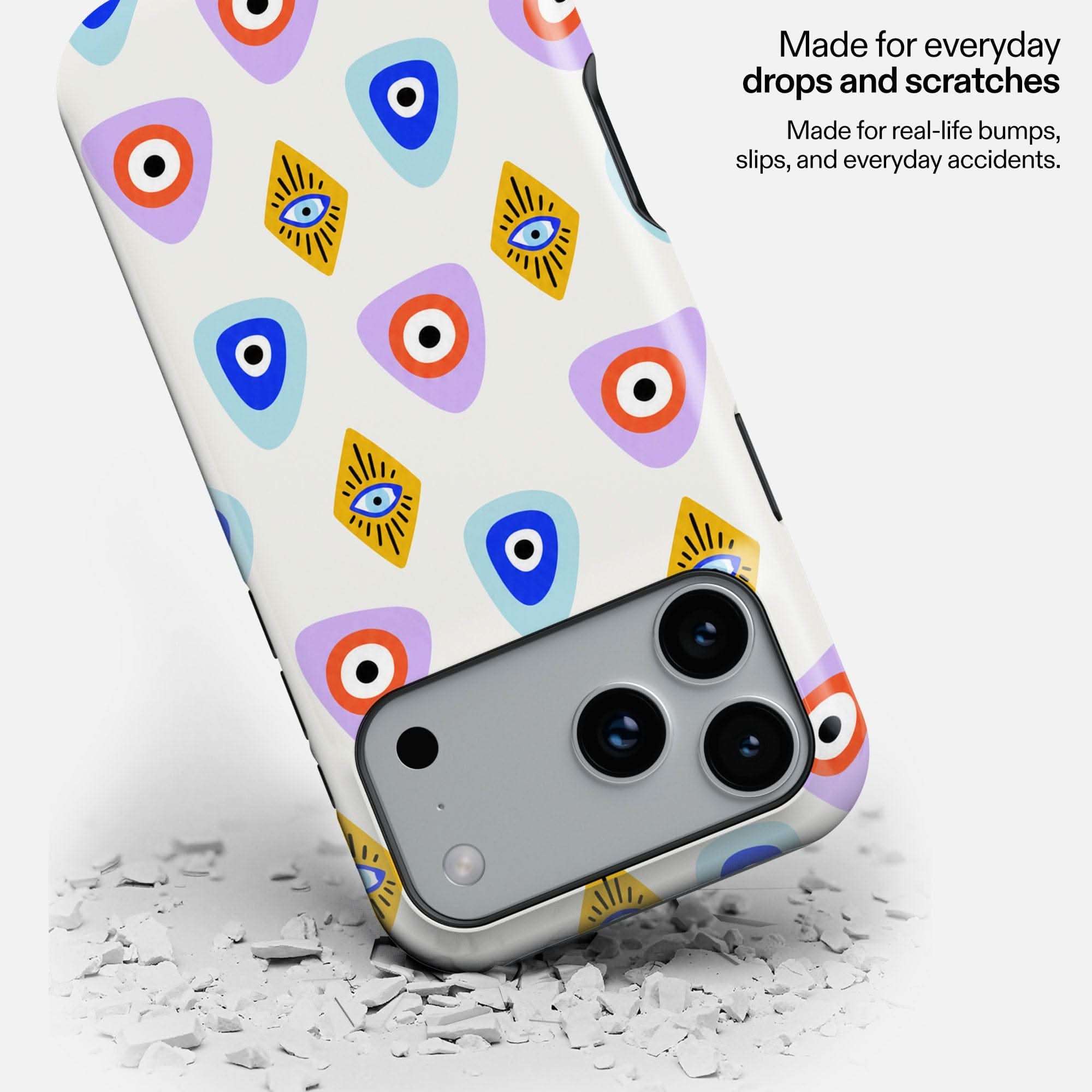 White phone case with colorful evil eye and geometric patterns, sitting on cracked surface.