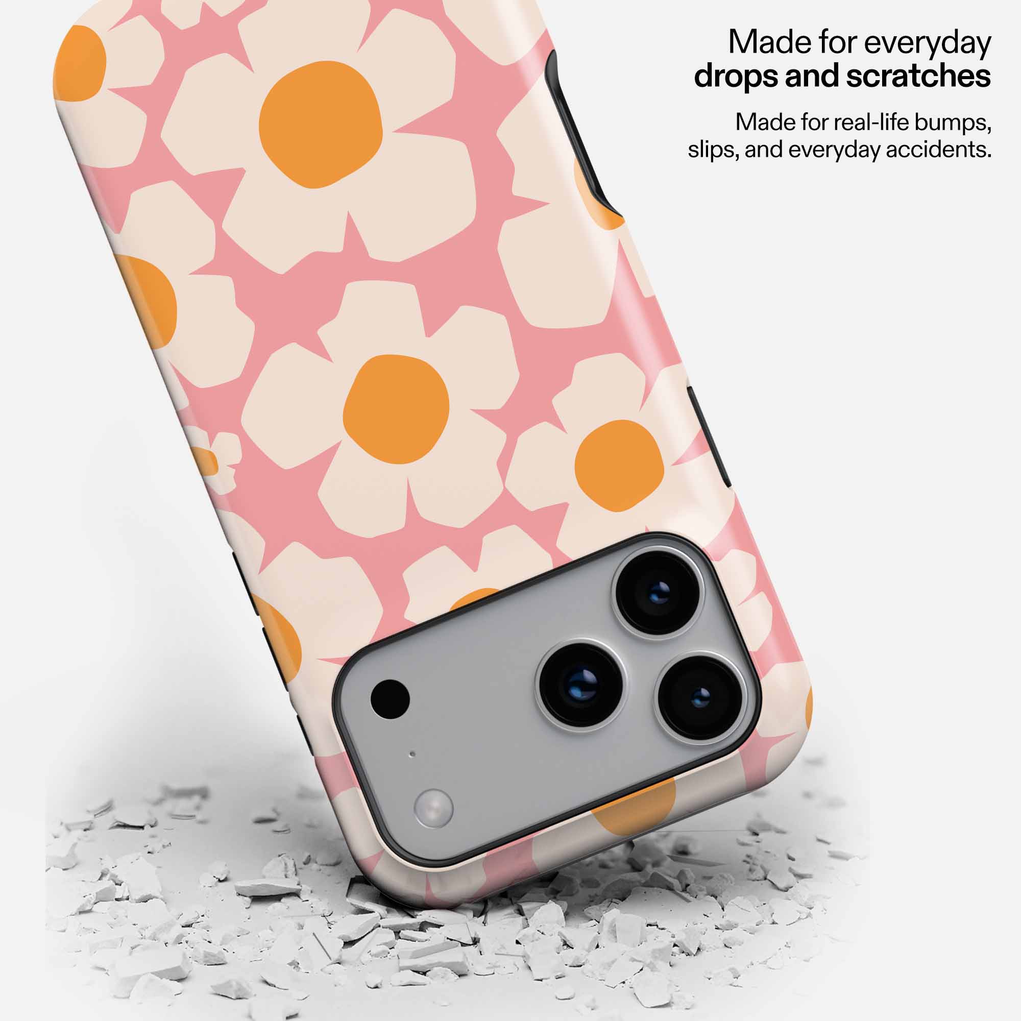 Pink floral phone case with white and orange flowers, dropped on concrete showing durability.
