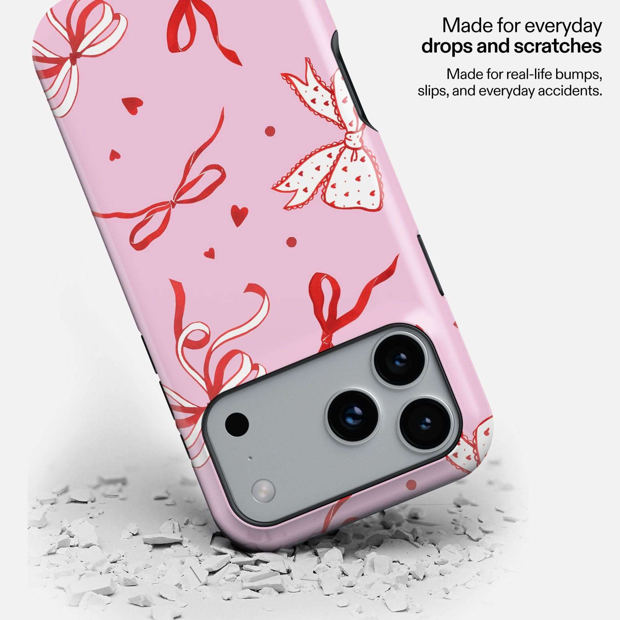 Pink MagSafe phone case with red ribbon and butterfly design, dropped on white debris to show durability.