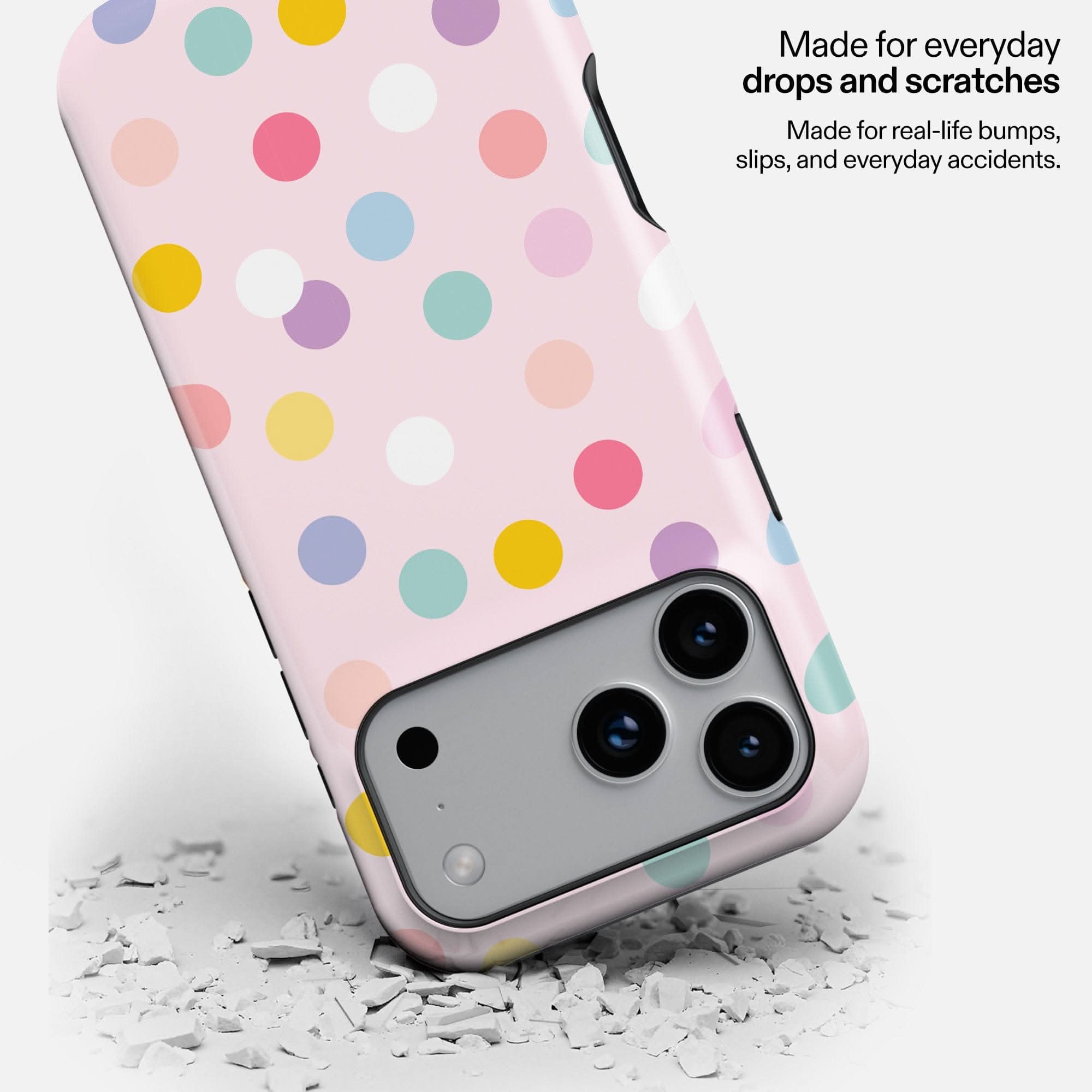 Pink polka dot phone case with colorful circles, shown dropped on white debris, demonstrating durability.