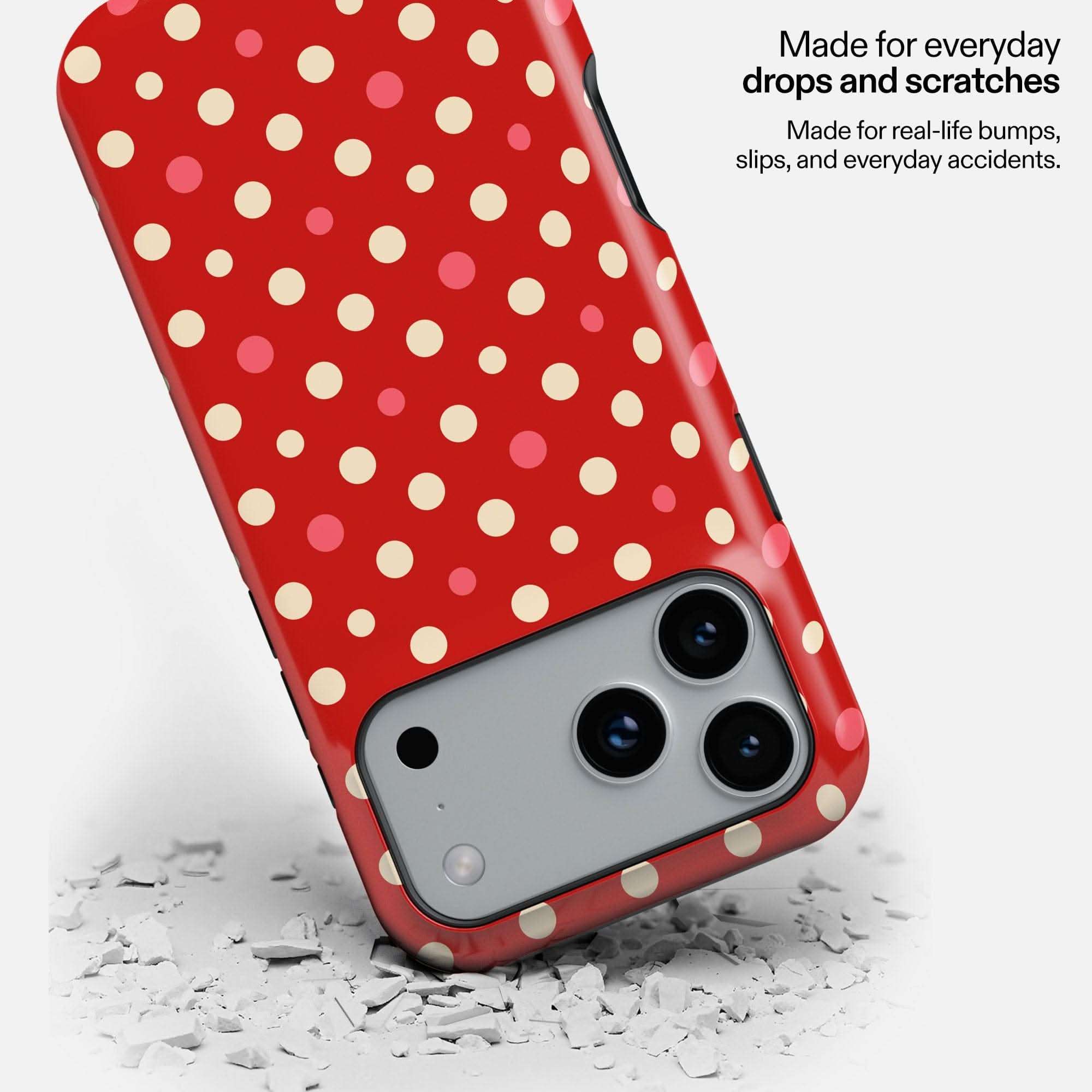 Red polka dot phone case with camera cutout dropped on white debris, demonstrating durability.