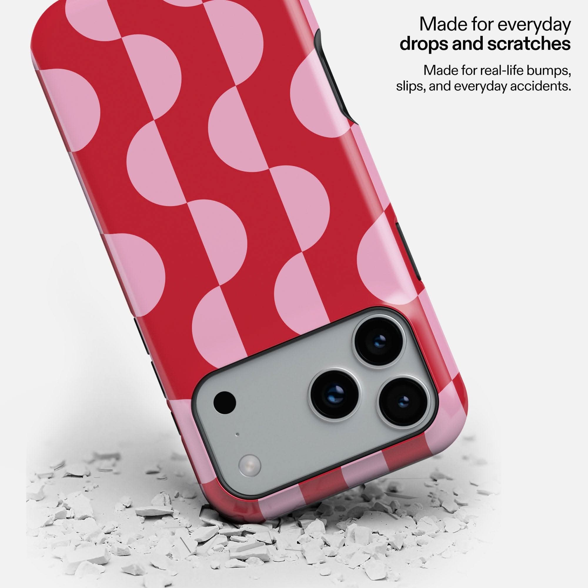 Red and pink polka dot MagSafe phone case with triple camera cutout, shown dropping onto concrete debris.