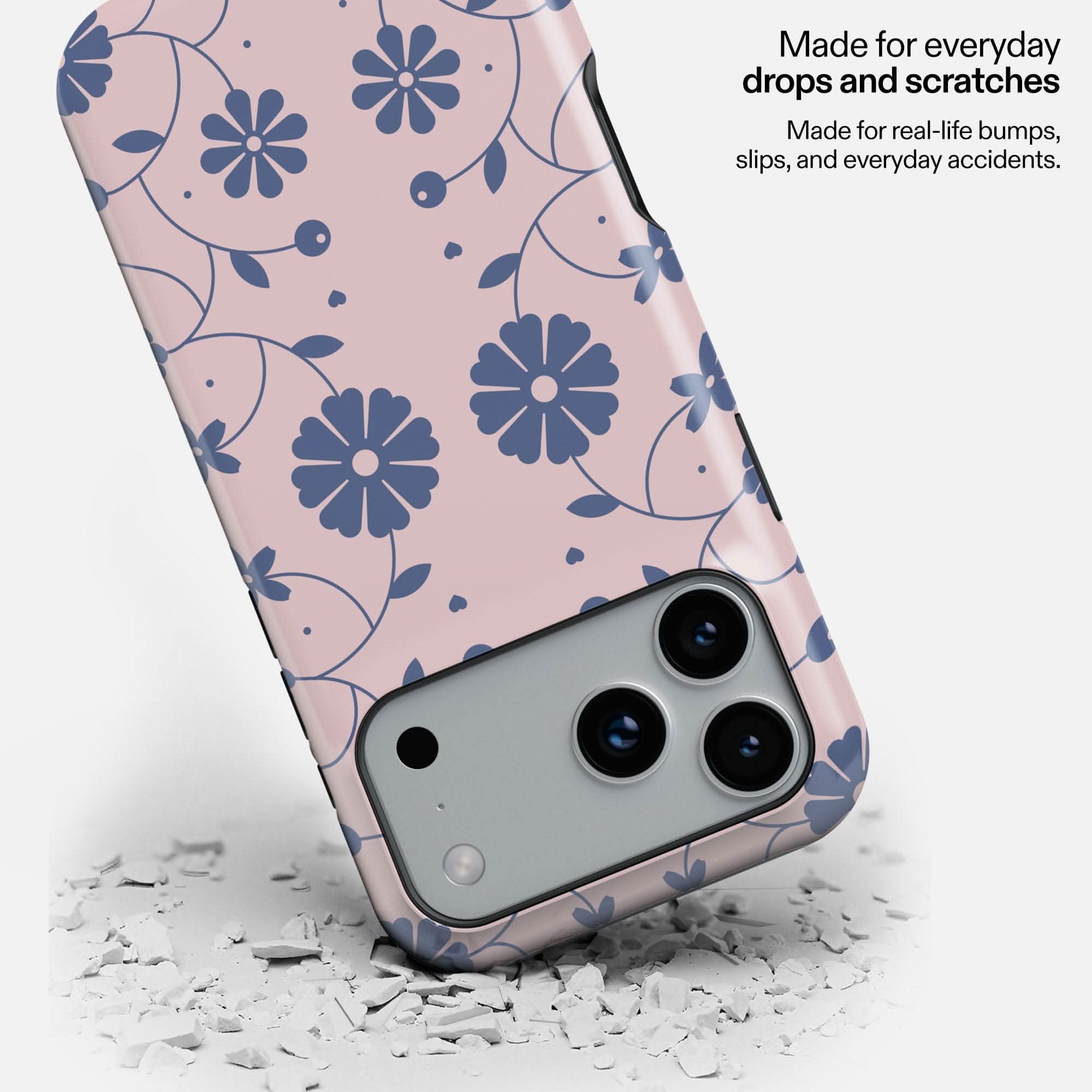 Pink phone case with navy floral pattern, featuring reinforced corners and camera protection on white debris.