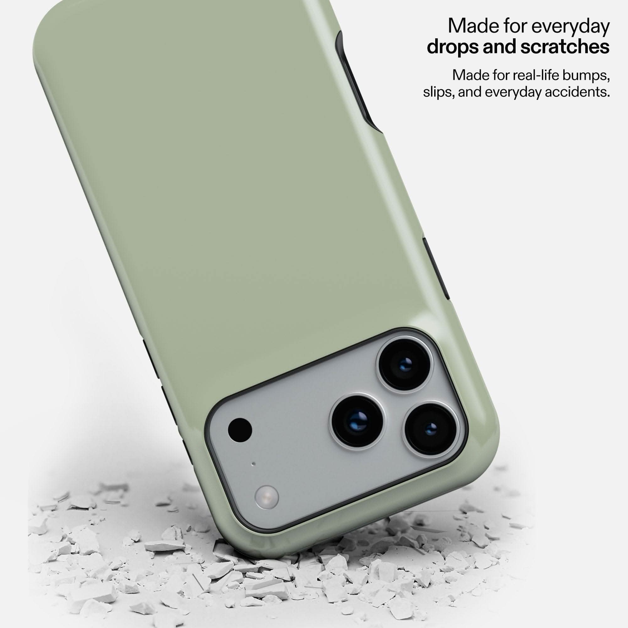 Sage green MagSafe tough phone case tilted on white debris, showing camera cutout and durability.