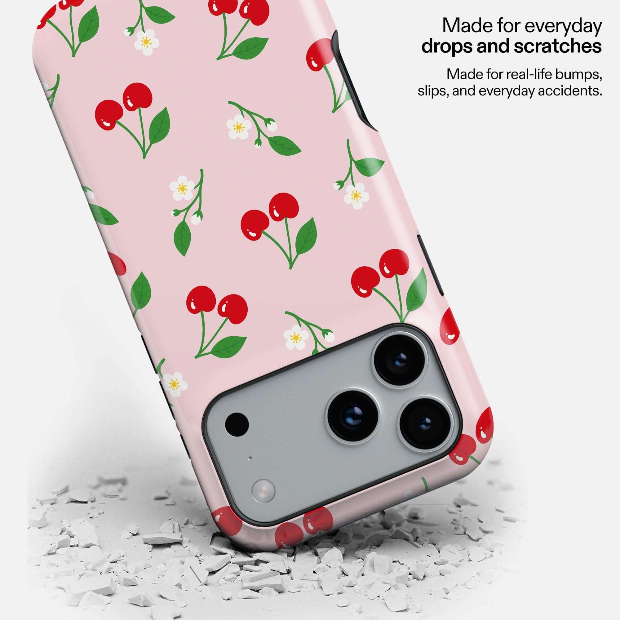 Cherry Summer MagSafe Tough Phone Case with red cherries and white flowers on pink background, shown dropped on concrete.